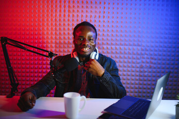 Young african american man recording or streaming podcast using microphone at his small broadcast...