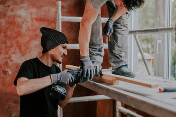 Two builders are sawing a board with an electric saw.