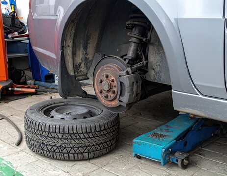 una auto sobre la gata sin una rueda, la rueda de repuesto a un lado