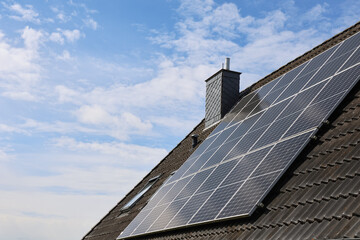 Photovoltaic panels providing green energy on a tiled roof under a cloudy sky