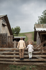 Two children are peeking over a fence on a farm. The boys are standing with their backs turned.