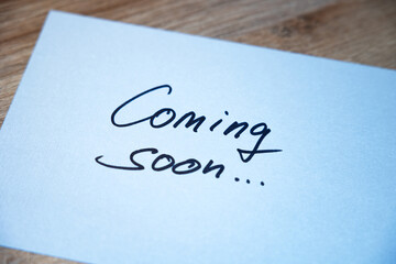 Coming soon. White note with handwritten text. Business,  announcement message, event.