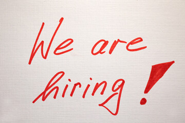 We are hiring! White note with handwritten text in red. Marketing, recruitment, job interview, occupation, vacancy, trainee, job fair.