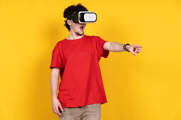 Young man exploring virtual reality with vr headset pointing finger on yellow background
