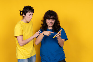 Two young women reacting to smartphone content on yellow background