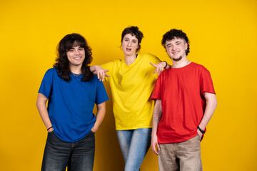 Three young adults pointing fingers to each other on yellow background