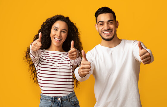 Best Choice. Portrait of happy middle eastern couple gesturing thumbs up at camera, cheerful arab man and woman showing sign of approvel while standing isolated over yellow background, copy space