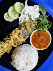 Pecel lele menu complete with fried catfish served with rice, cabbage leaves, sliced ​​cucumber and chili sauce ready to eat.