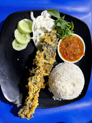 Pecel lele menu complete with fried catfish served with rice, cabbage leaves, sliced ​​cucumber and chili sauce ready to eat.