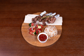lamb square, lamb meat, Turkish rice with meat and adjika, mixed salad, and vegetable salad on the table in the restaurant on a wooden stand