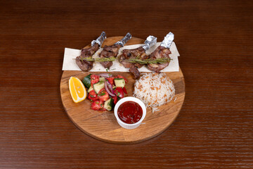 lamb square, lamb meat, Turkish rice with meat and adjika, mixed salad, and vegetable salad on the table in the restaurant on a wooden stand