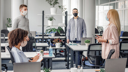 Obraz premium Meeting and new tasks from manager during covid-19 epidemic. Woman in business suit and protective mask speaks with workers, african american lady takes notes in office interior, panorama, empty space