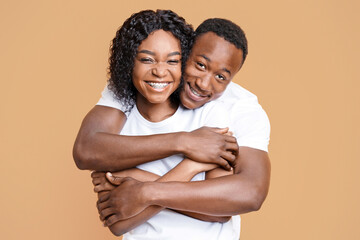 Obraz premium Loving black couple cuddling over yellow studio background. Cheerful young african american man and woman hugging and smiling at camera. Love, relationships, marriage concept