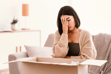 Wrong Parcel. Unhappy frustrated asian woman unpacking box sad with bad delivery service sitting on...