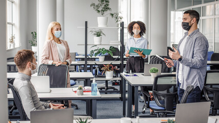 Social distancing in public place, disease prevention during quarantine, staff safety. Meeting and reporting on project or team building by employees and boss in office interior with devices