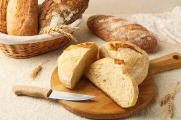 Different types of fresh bread, knife and spikelets on light textured table, closeup