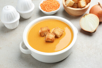 Delicious lentil cream soup served with croutons on light grey table, closeup