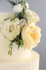 Delicious wedding cake decorated with flowers on grey background, closeup