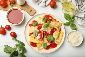 Delicious ravioli with tomato sauce, parmesan cheese and basil on white table, flat lay