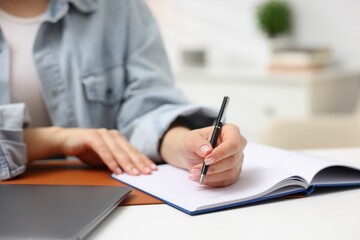 Woman writing in planner at white desk indoors, closeup. Space for text