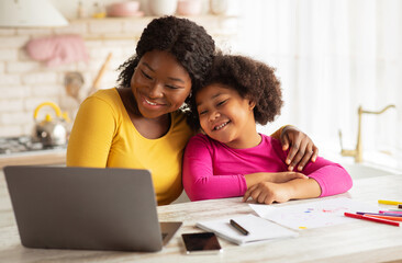 Obraz premium Happy African American Mom And Her Cute Little Daughter Using Laptop Together In Kitchen, Black Family Having Fun At Home, Embracing And Watching Cartoons Or Kids Development Videos Online, Free Space