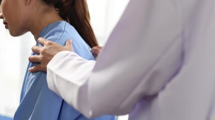 Professional female physician listening to patient's lungs during medical examination, carefully checking respiratory health in clinical office.