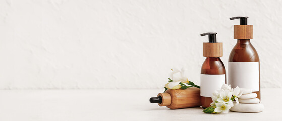 Bottles of cosmetic products, spa stones and flowers on light background