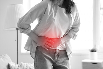 Young woman suffering from severe abdominal pain at home, closeup