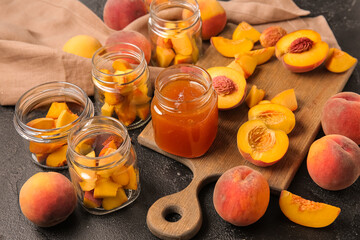 Jars with sweet peach jam and fresh fruits on black background
