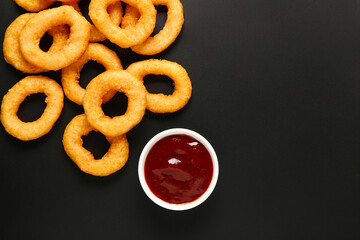 Fried breaded onion rings with ketchup on black background