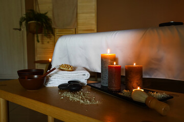 Burning candles with sea salt on table in dark spa salon, closeup