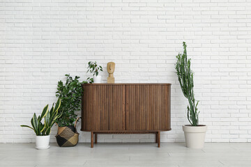 Big cactus with houseplants, home decor and commode near white brick wall in room