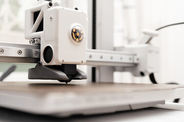 Close up and low angle shot of white modern design 3D printer nozzle head on build plate ready to print. Product design, STEM education, technology, maker concept.