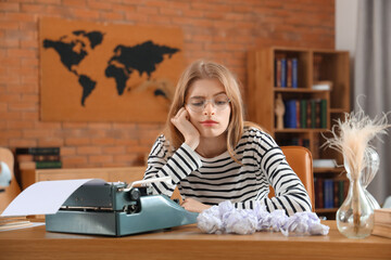Tired female author with vintage typewriter at table in office
