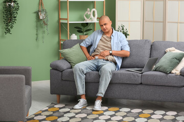 Young man with medical patch after appendix surgery sitting on sofa at home