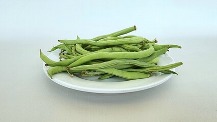 baby green beans or mini green beans on a white plate, isolated on white background