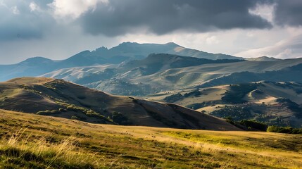 Obraz premium Vast Mountain Landscape Under Cloudy Sky With Golden Sunlight and Green Hills