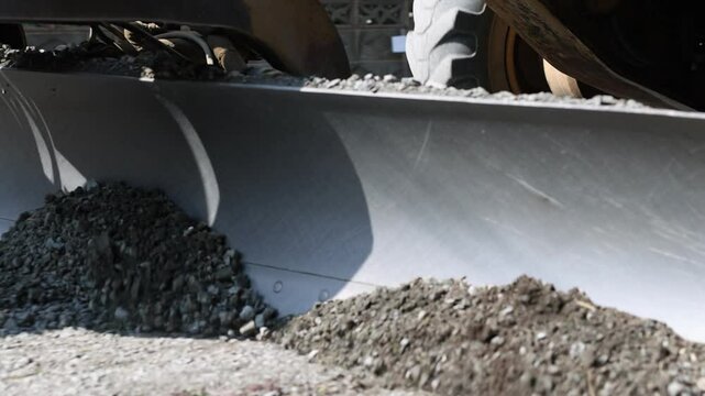 Heavy machinery, grader leveling gravel on construction site, preparing ground for road infrastructure development.