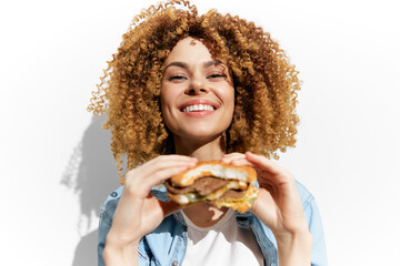 Happy woman with curly hair enjoys a delicious burger, showcasing summer vibes and healthy eating...