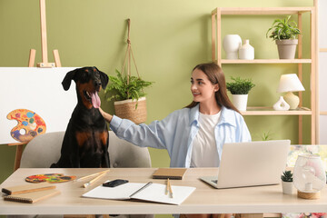 Cute Doberman dog and beautiful young happy woman with paints palettes working at home