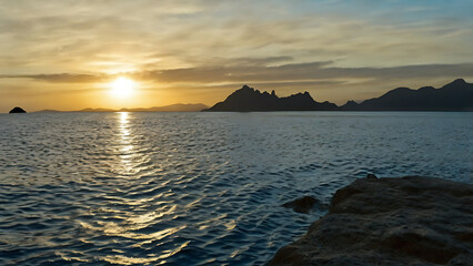 Stunning sunset over the ocean with mountain silhouettes and water reflections.