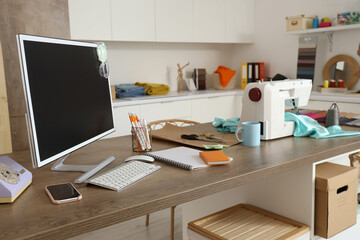 Fashion designer's workplace with computer monitor and sewing supplies in studio