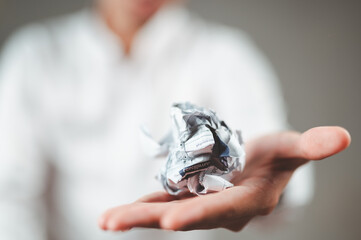 A businessman in a white suit crumples a piece of paper and holds it out in front of him.