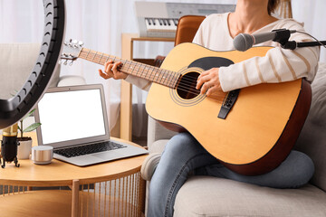 Female blogger playing guitar on sofa at home