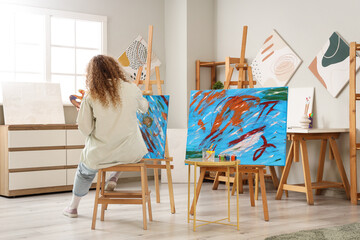 Female artist painting on canvas in workshop, back view