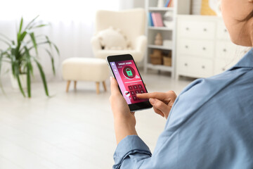 Young woman using mobile phone with smart home security system application in room, closeup