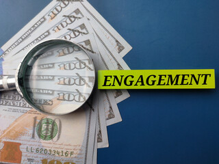 Banknotes and magnifying glass with the word ENGAGEMENT on a blue background
