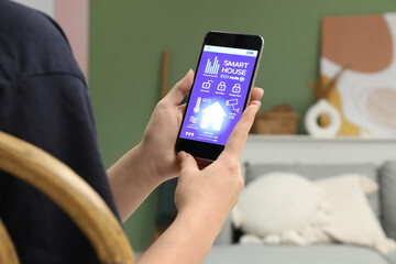 Young woman using smart home security system application on mobile phone in room, closeup