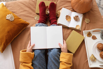 Fototapeta premium Woman with blank books and autumn leaves sitting on bed, top view