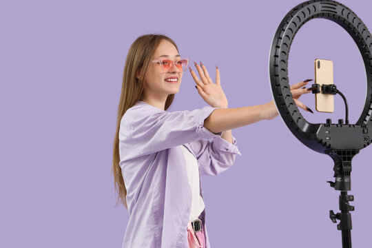 Female blogger recording video on lilac background